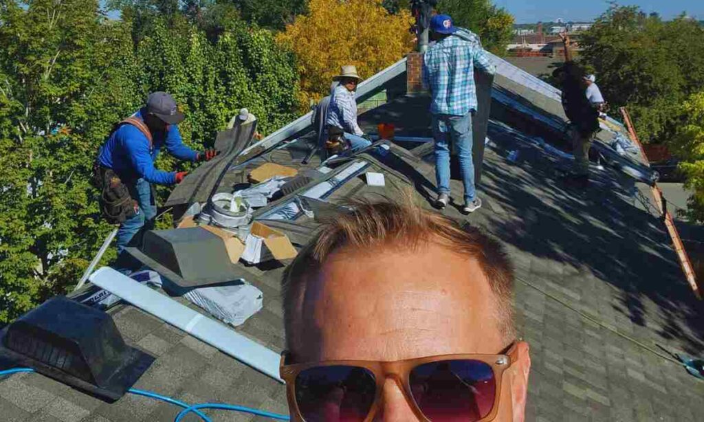Team of roofers working on shingle installation with tools, vents, and materials spread across a residential roof in Denver, while homeowner observes from below