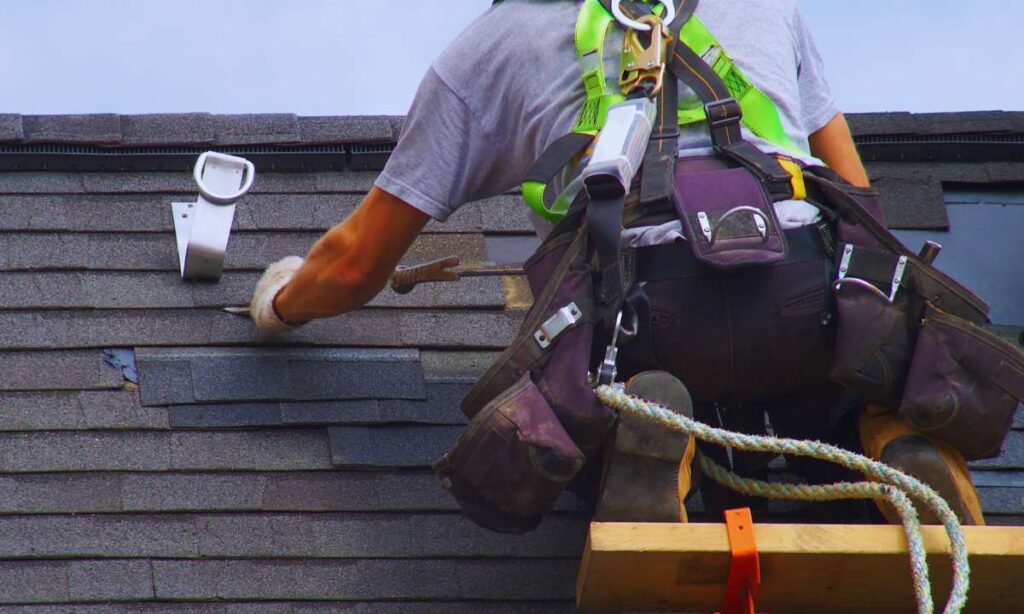 Professional roofer wearing a safety harness while replacing asphalt shingles on a steep Denver roof, illustrating skilled repairs often tied to insurance deductible claims.