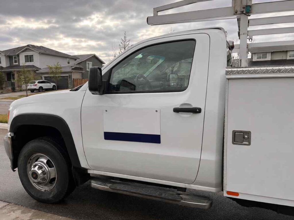 Out-of-state license plate and non-local phone number on work truck door panel parked in Front Range neighborhood